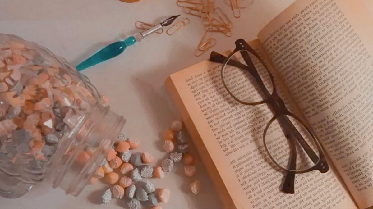Header image for the What I Want To Do After Graduation blog post. The image contains an open book on the left side of the image with glasses on it as well as a blue fountain pen and a jar of spilled candy on the left side of the image. The picture has a pink hue. Also used on home page for print portfolio.