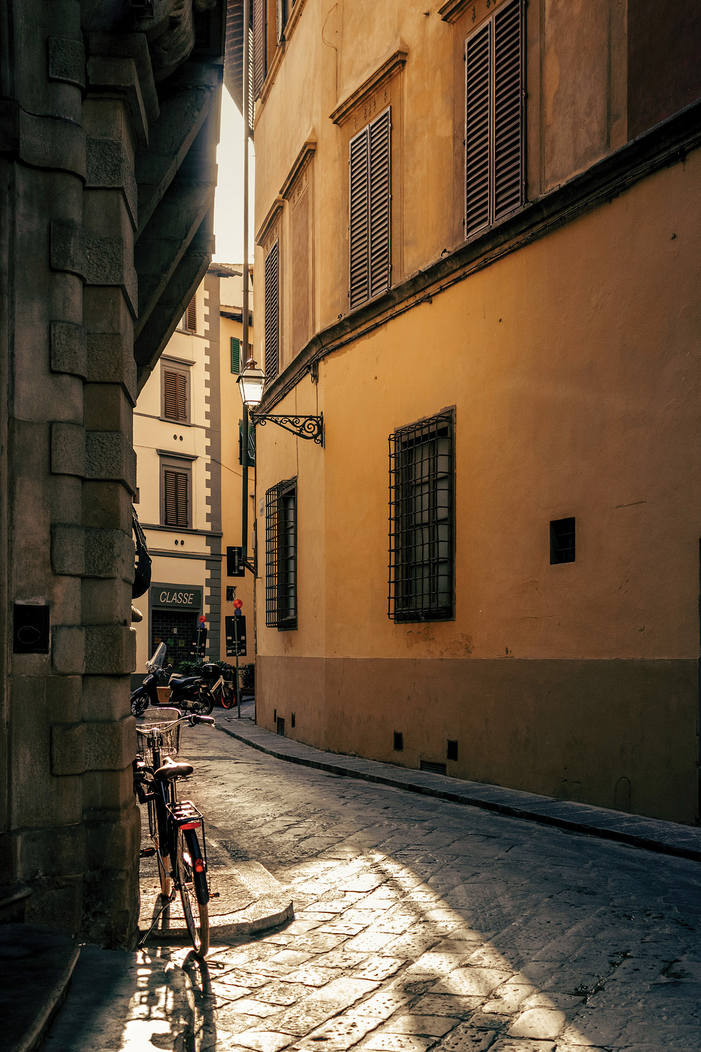 This acts as an example of an image after proper editing. It depicts a small alley with the first rays of sun shining through and illuminating a bike in the corner.