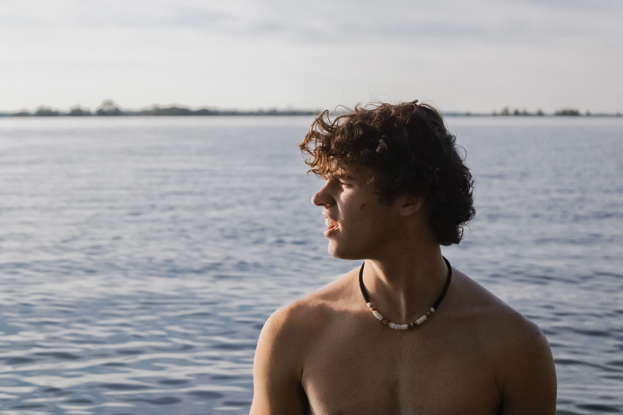 This acts as an example of an image before proper editing. It depicts a teen at a lake with sun shining on him.