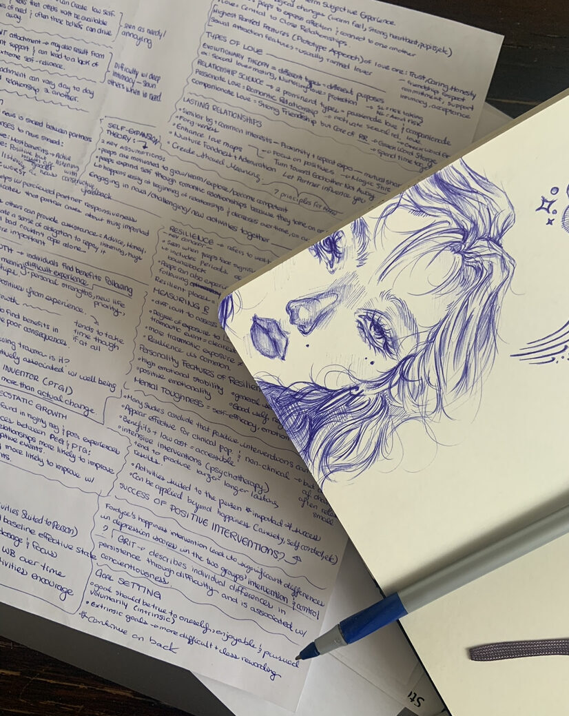Blue sketch on a notebook with notes on a sheet of paper in the background.