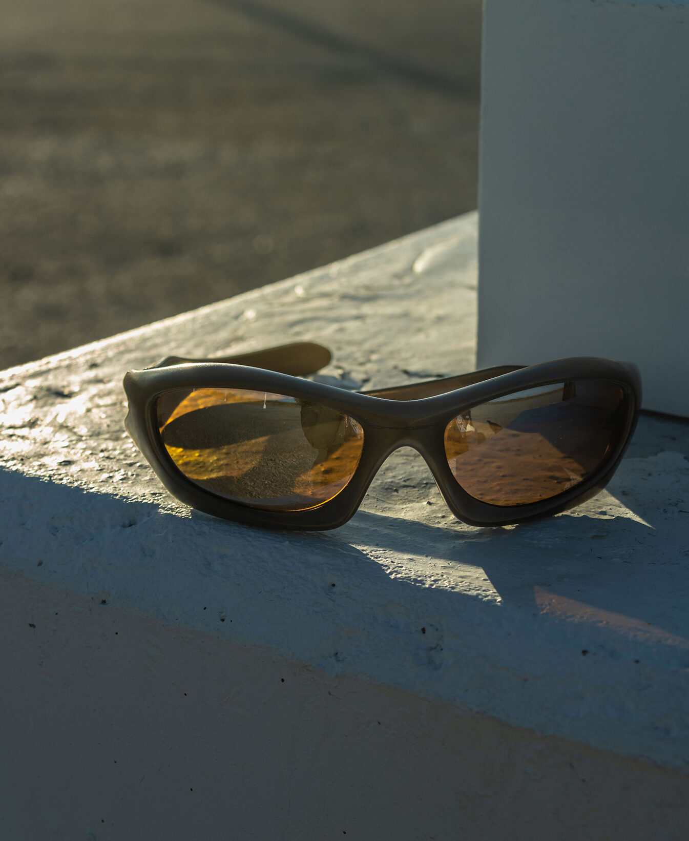 Sunglasses sit on a textured white ledge with sun shining through them.