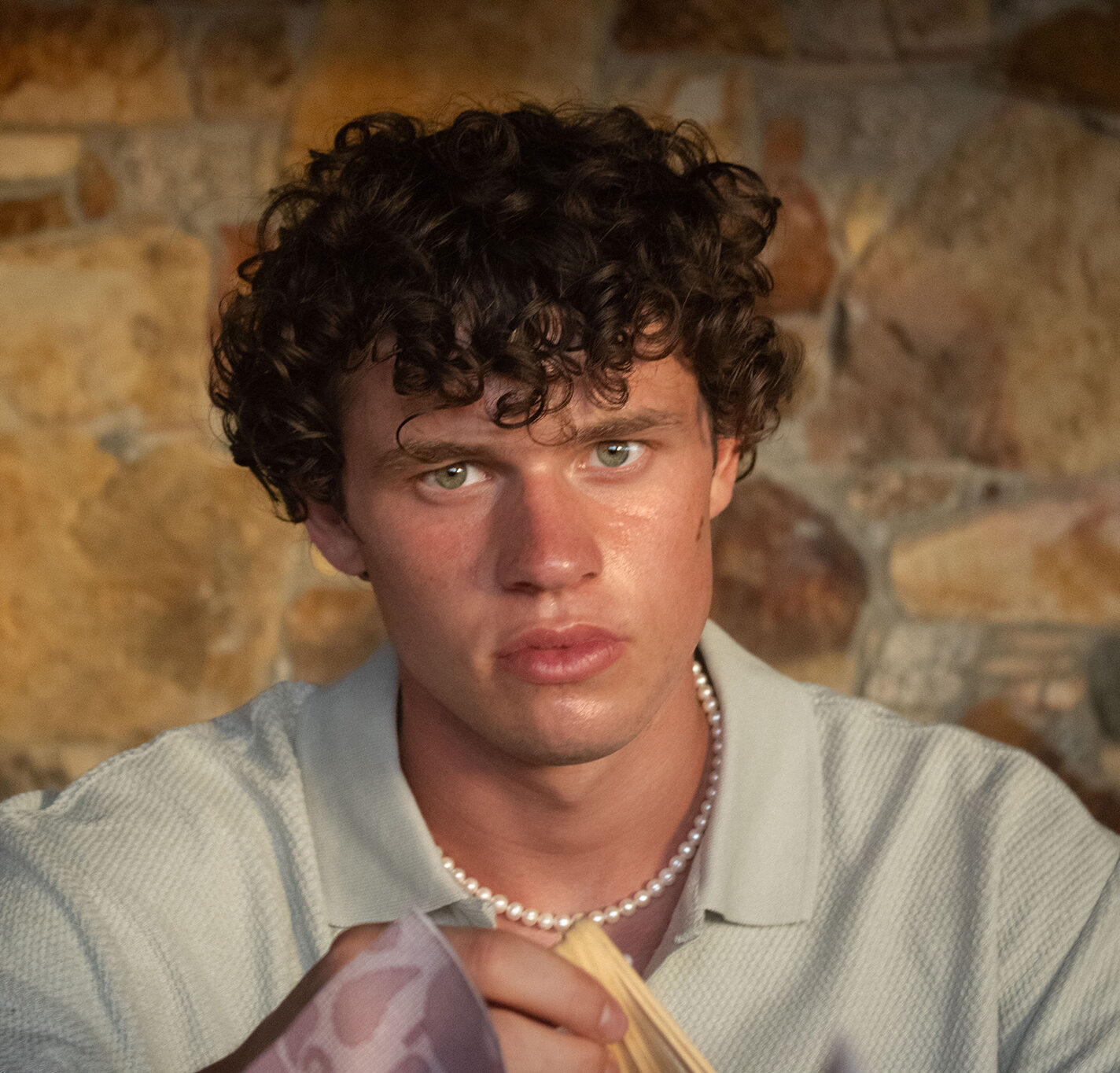 A young boy with curly hair looks intensely into the camera on a stone wall background.