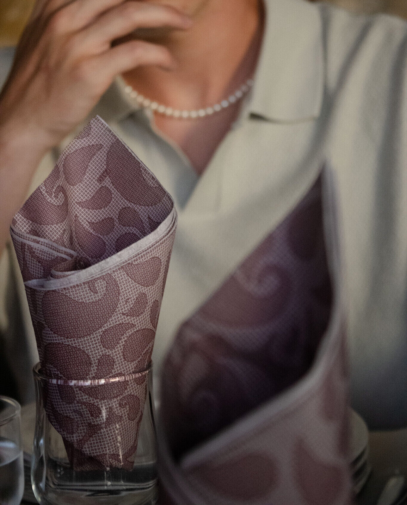 Two napkins folded in glasses stand in focus while a blurry figure sits behind them in a nice atmospheric shot.