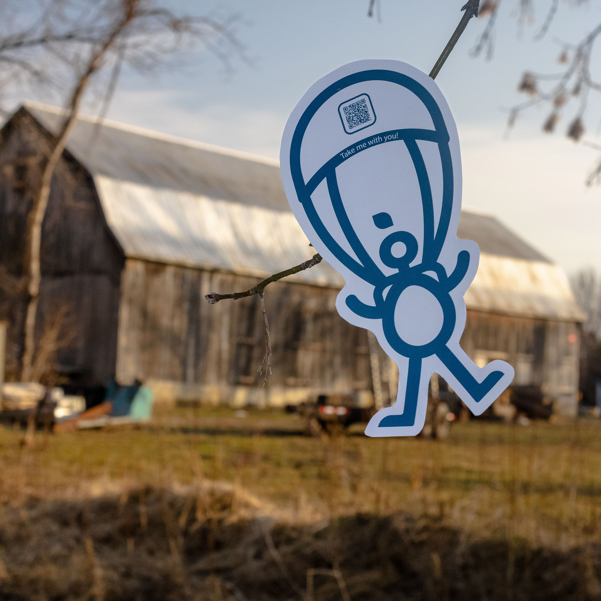 Cut out of Illo Adventures mascot Milo with a parachute on a country backdrop.